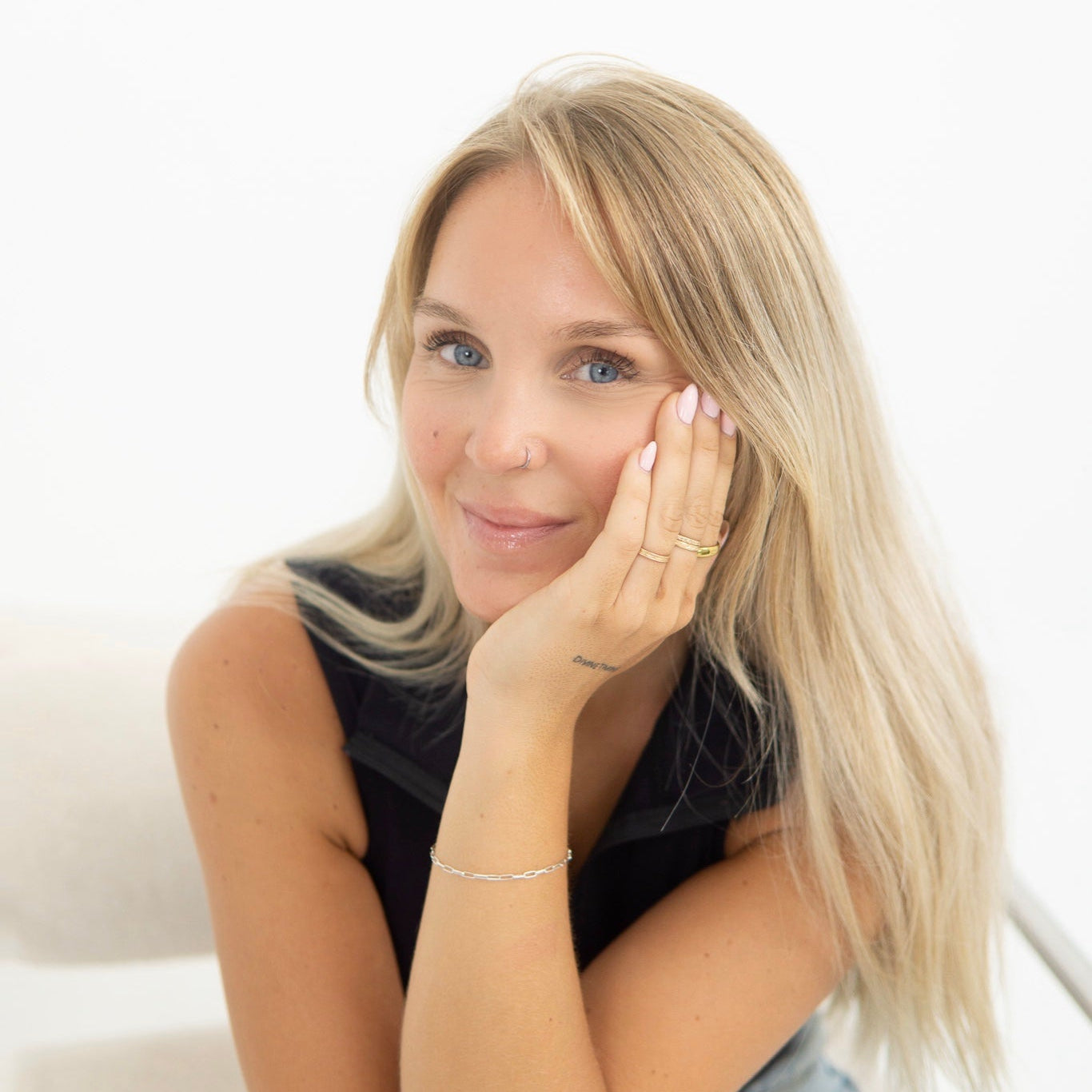 Woman with blonde hair and a black top sitting on a white couch.